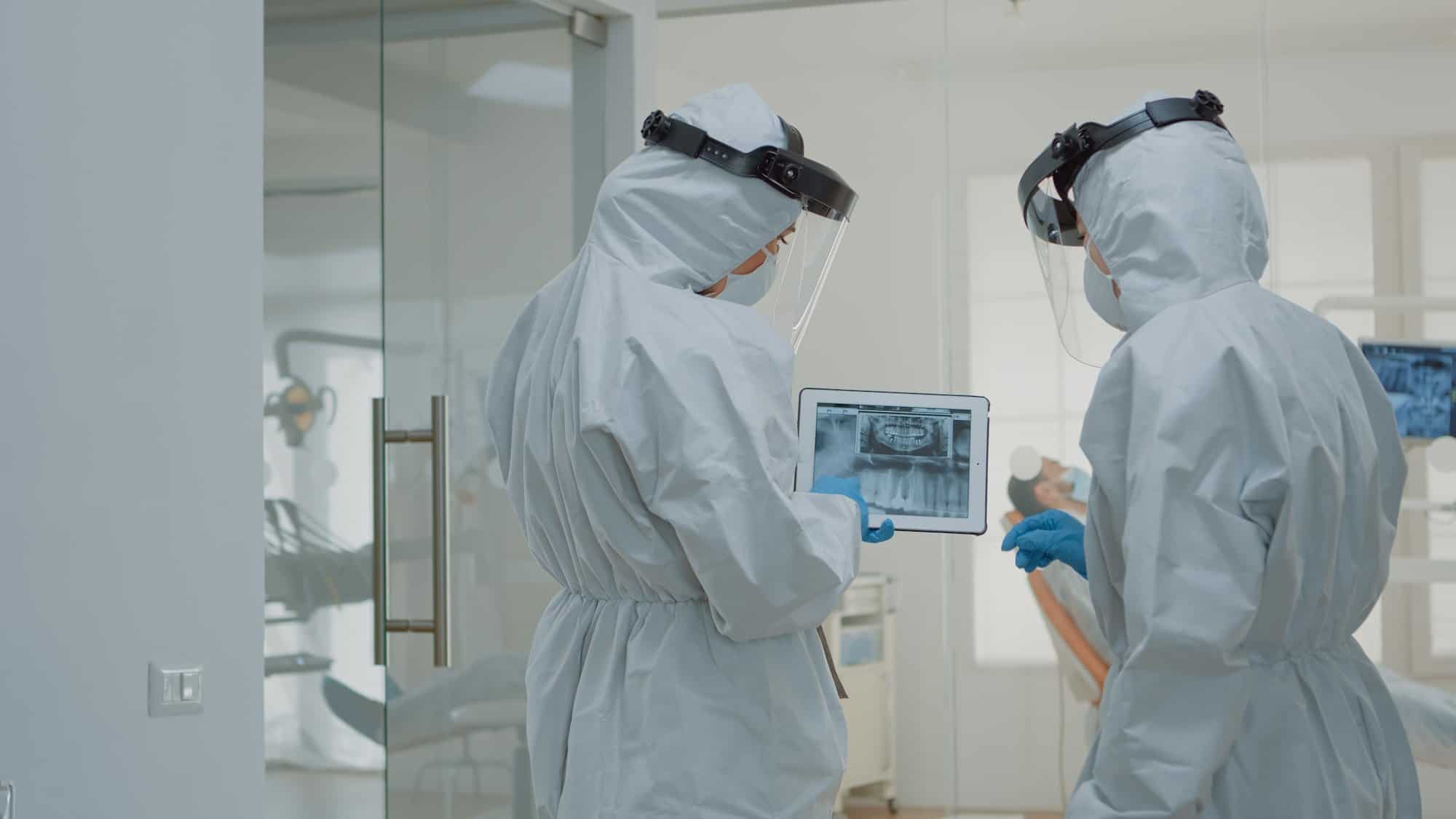 Stomatologists with ppe suits holding digital tablet with teeth x ray